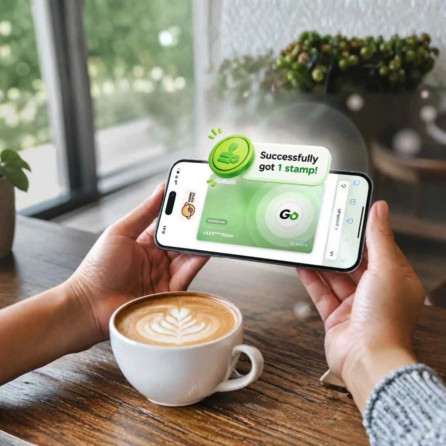 A hand holding a phone showing the GoBalik app confirming a successfully earned stamp, next to a latte